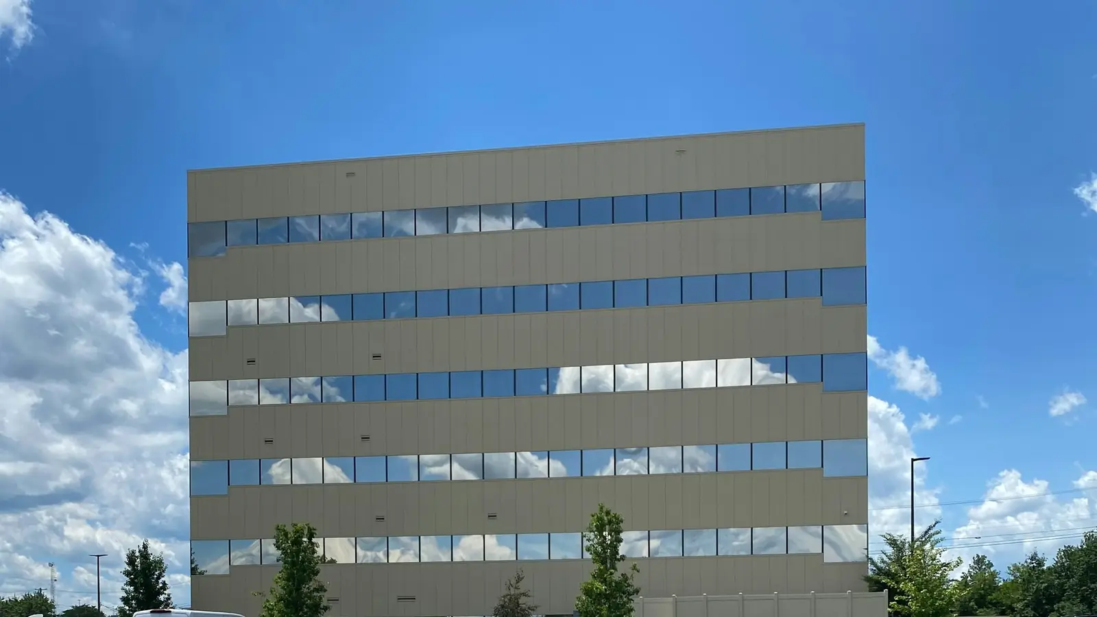 Modern kantoorgebouw met spiegelende ramen en een parkeerplaats ervoor